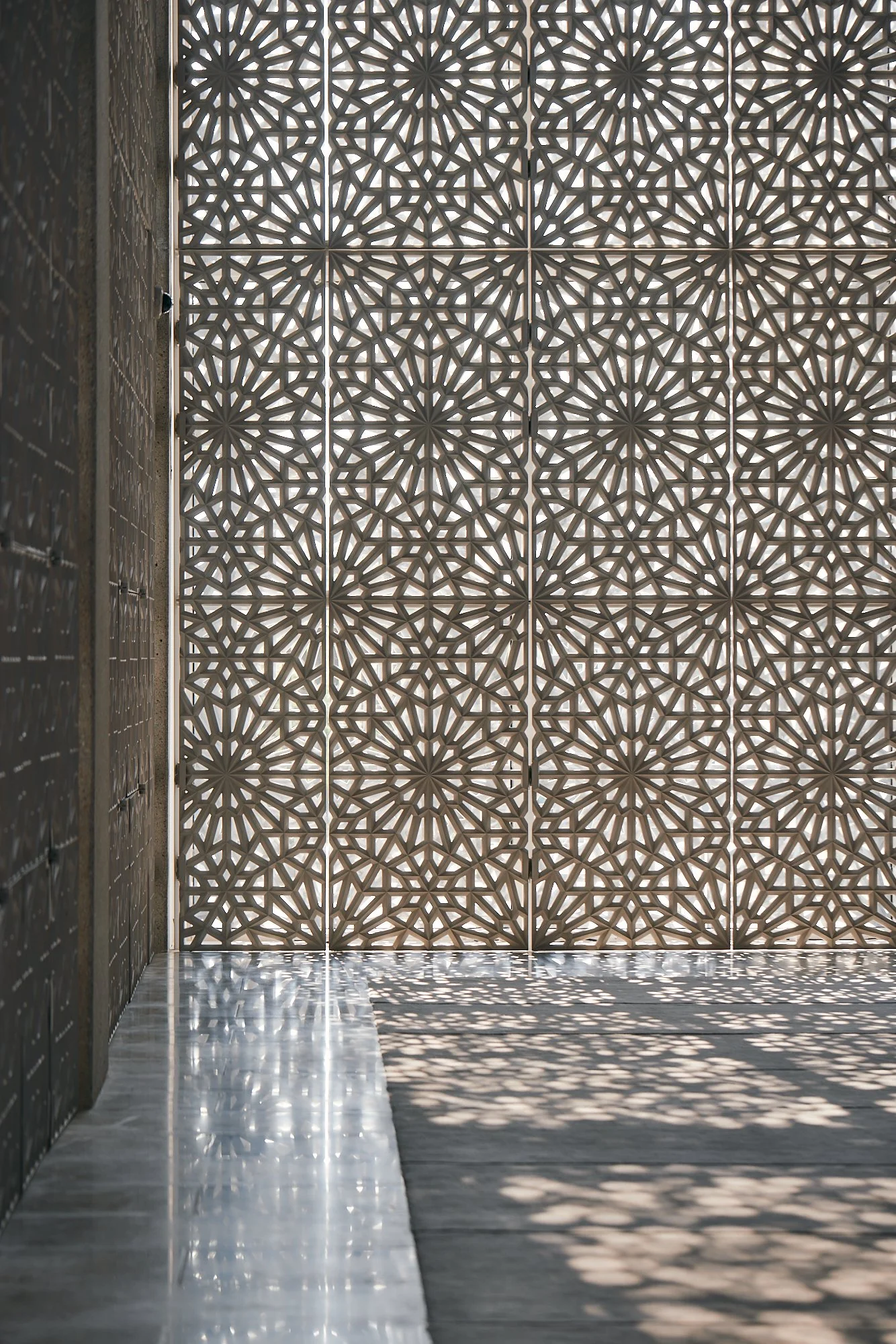 Decorative wall with intricate geometric pattern casting shadows on the floor.