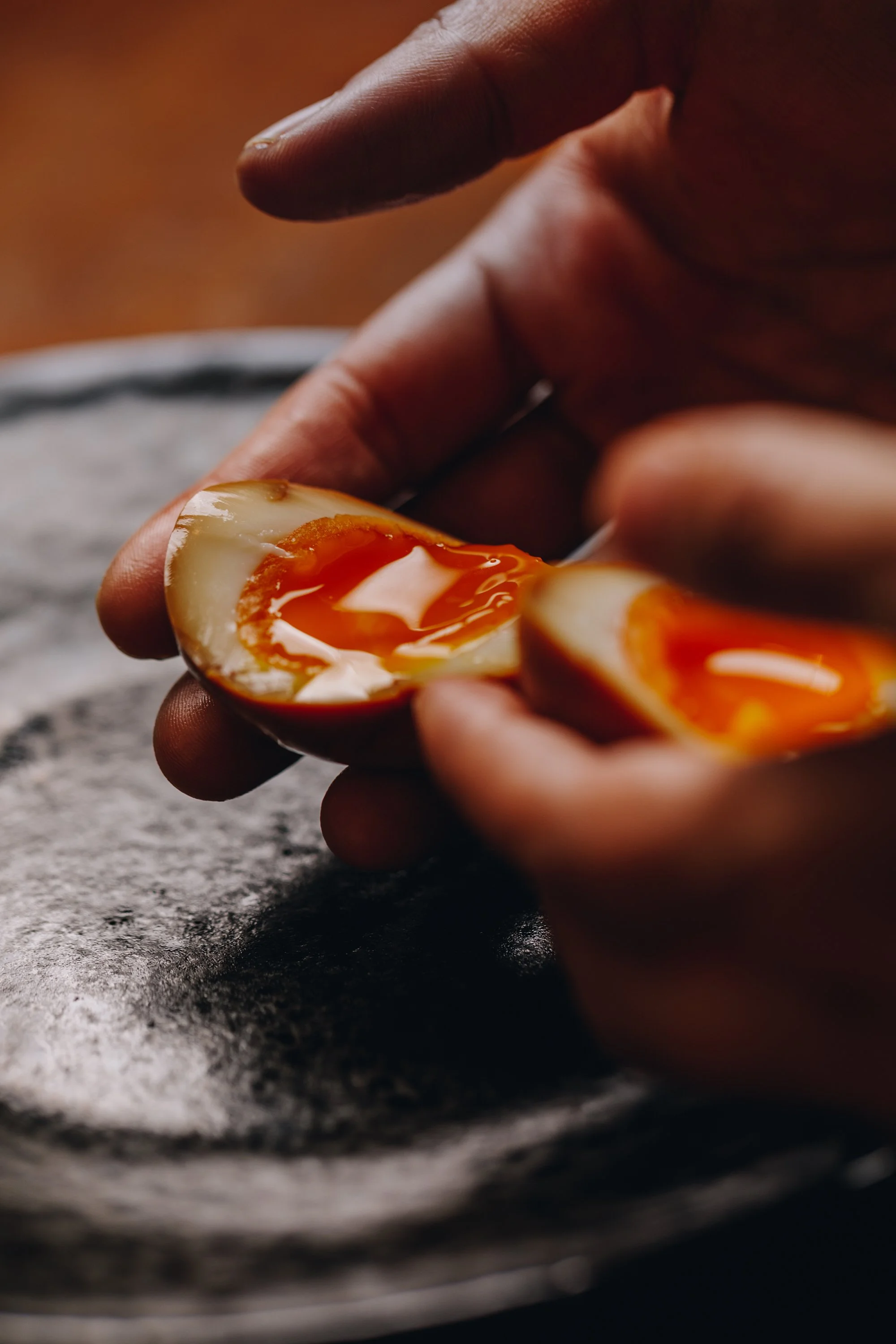 Close-up of a person cracking open a soft-boiled egg, showing the runny yolk inside.