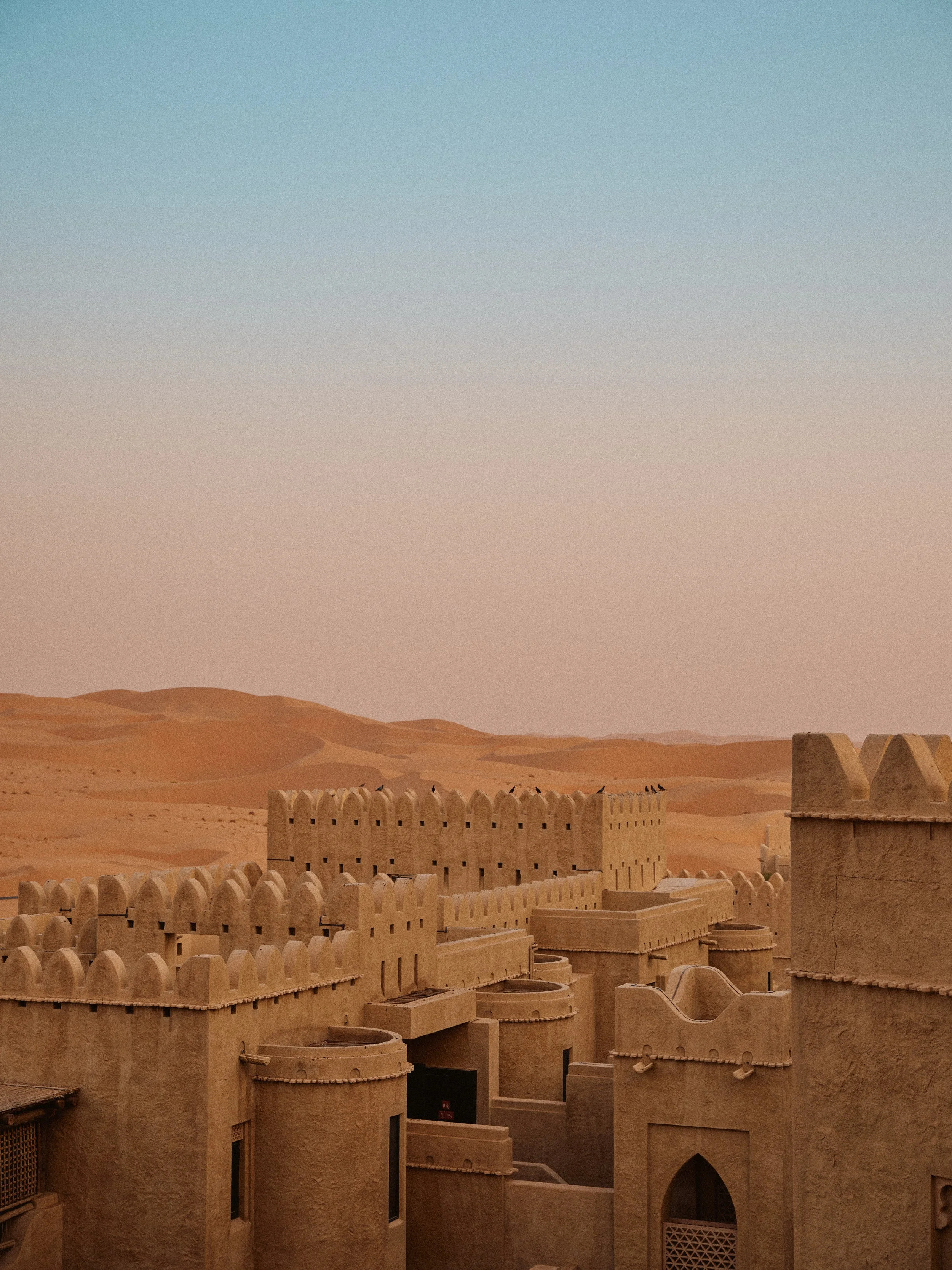 Sand dunes and fortress walls in a desert landscape under a clear sky.