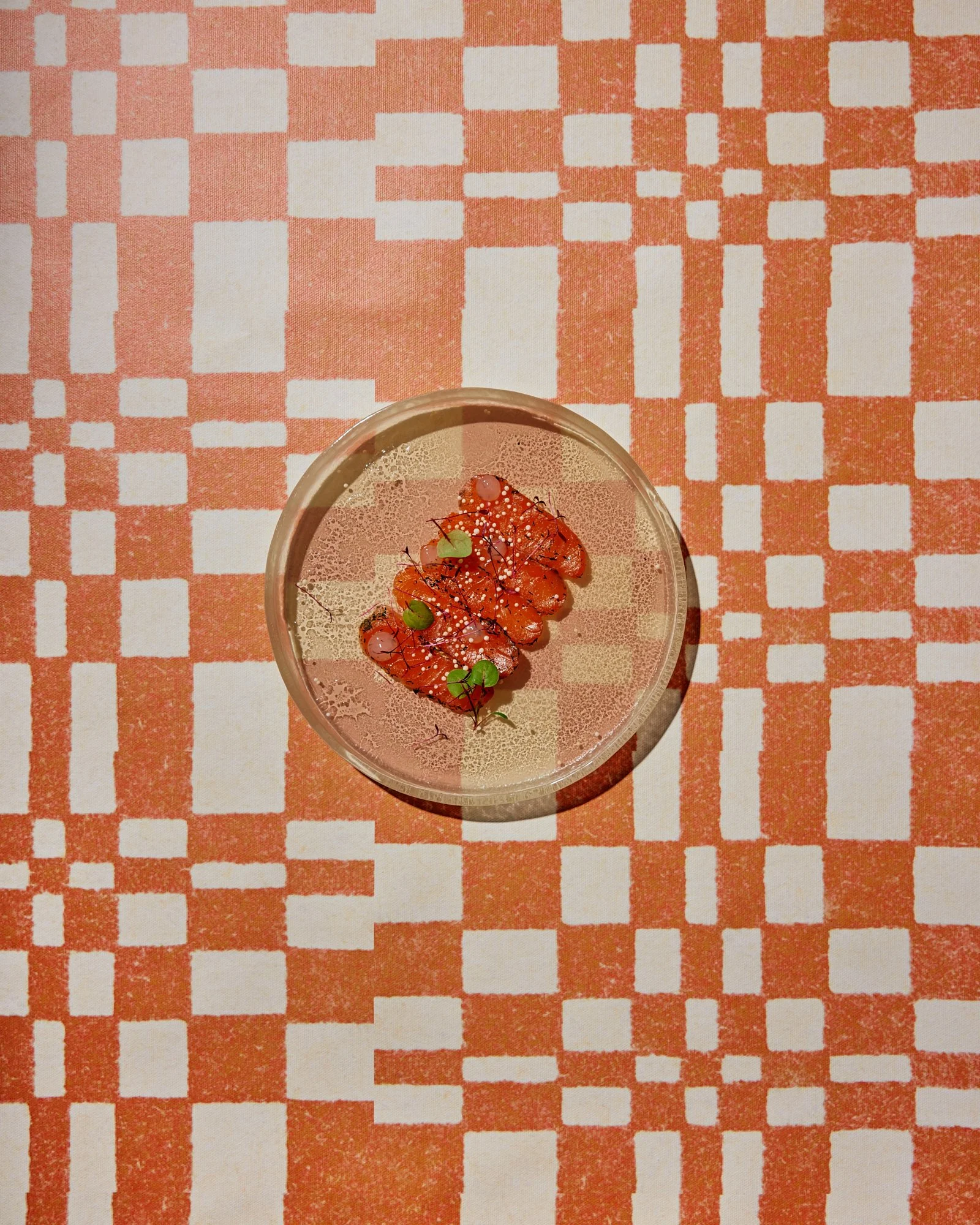 Glass of wine with salmon, microgreens, and white sesame seeds, on a patterned orange and white tablecloth.