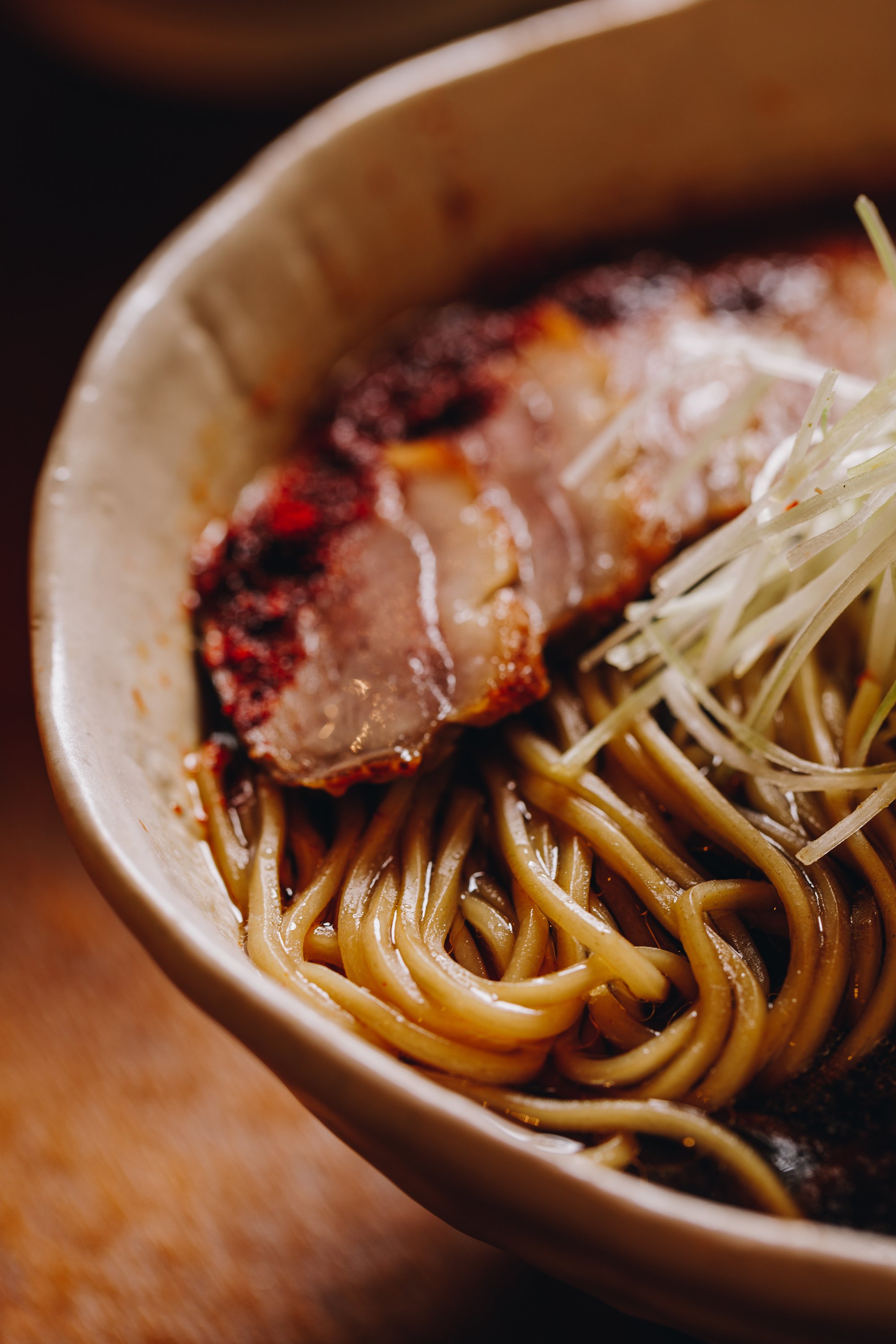 Close-up of Asian noodle bowl with grilled pork slices and shredded vegetables.