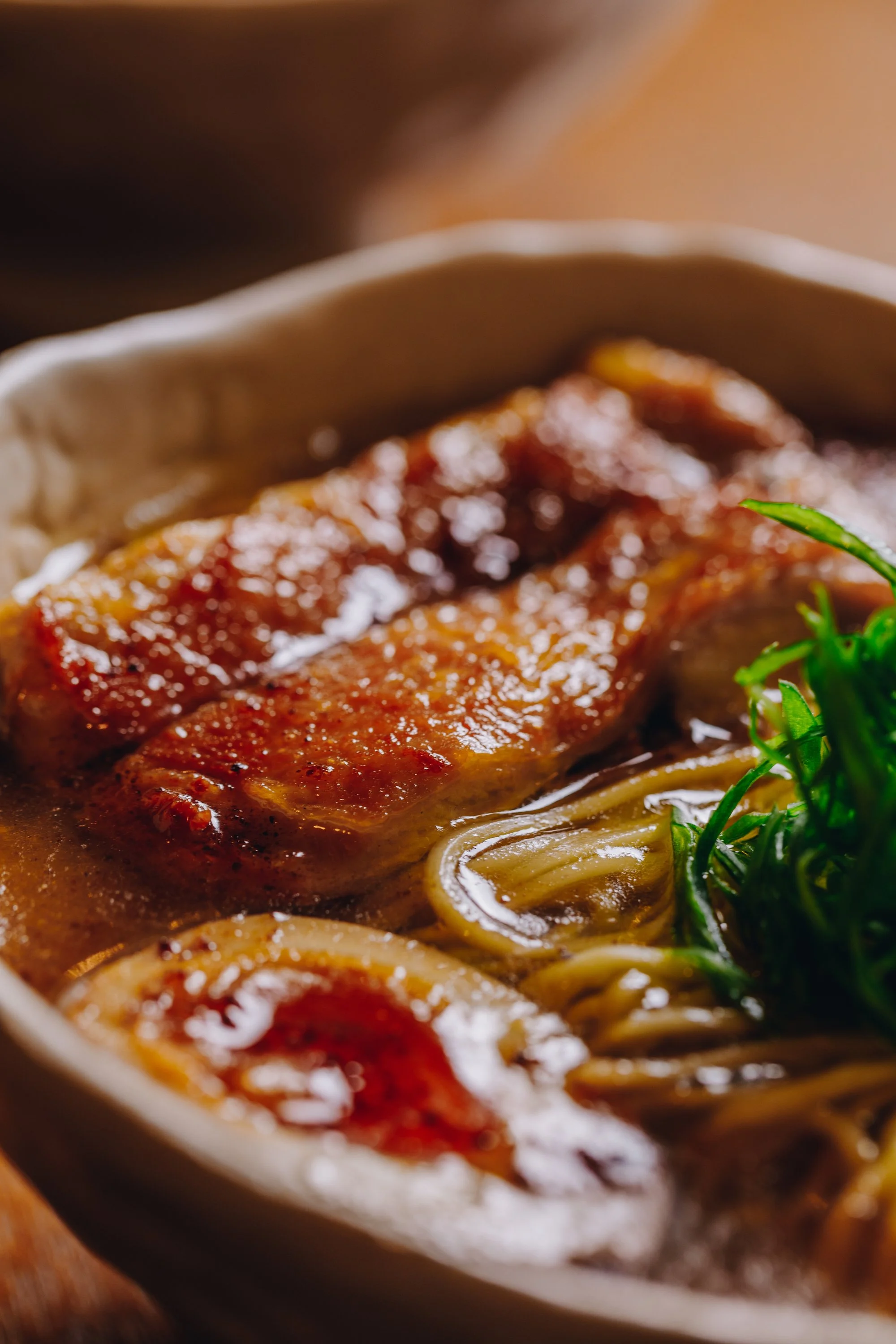Close-up of a bowl of ramen soup with a piece of pork belly, soft-boiled eggs, and green vegetables.