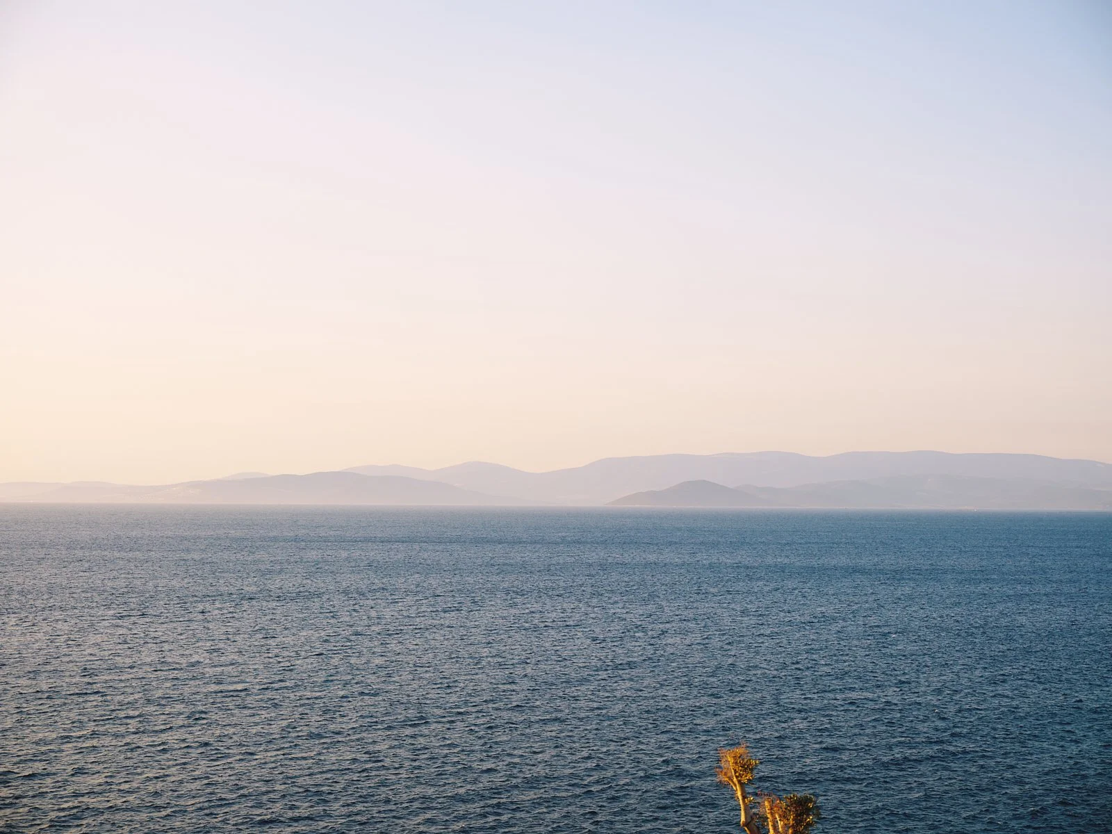 Calm sea with distant mountains and a clear sky.