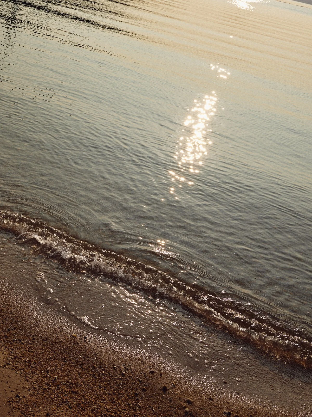 Photo of a beach with gentle waves and sunlight reflections on the water surface.