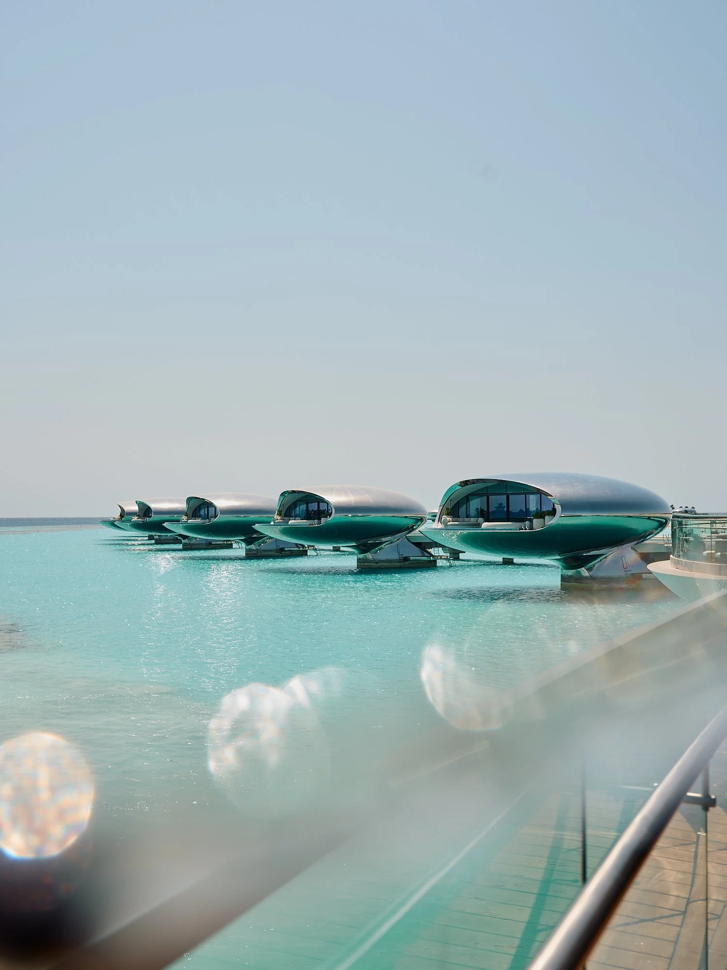 A row of futuristic, pod-like buildings on the water, with clear glass windows and curved metallic roofs