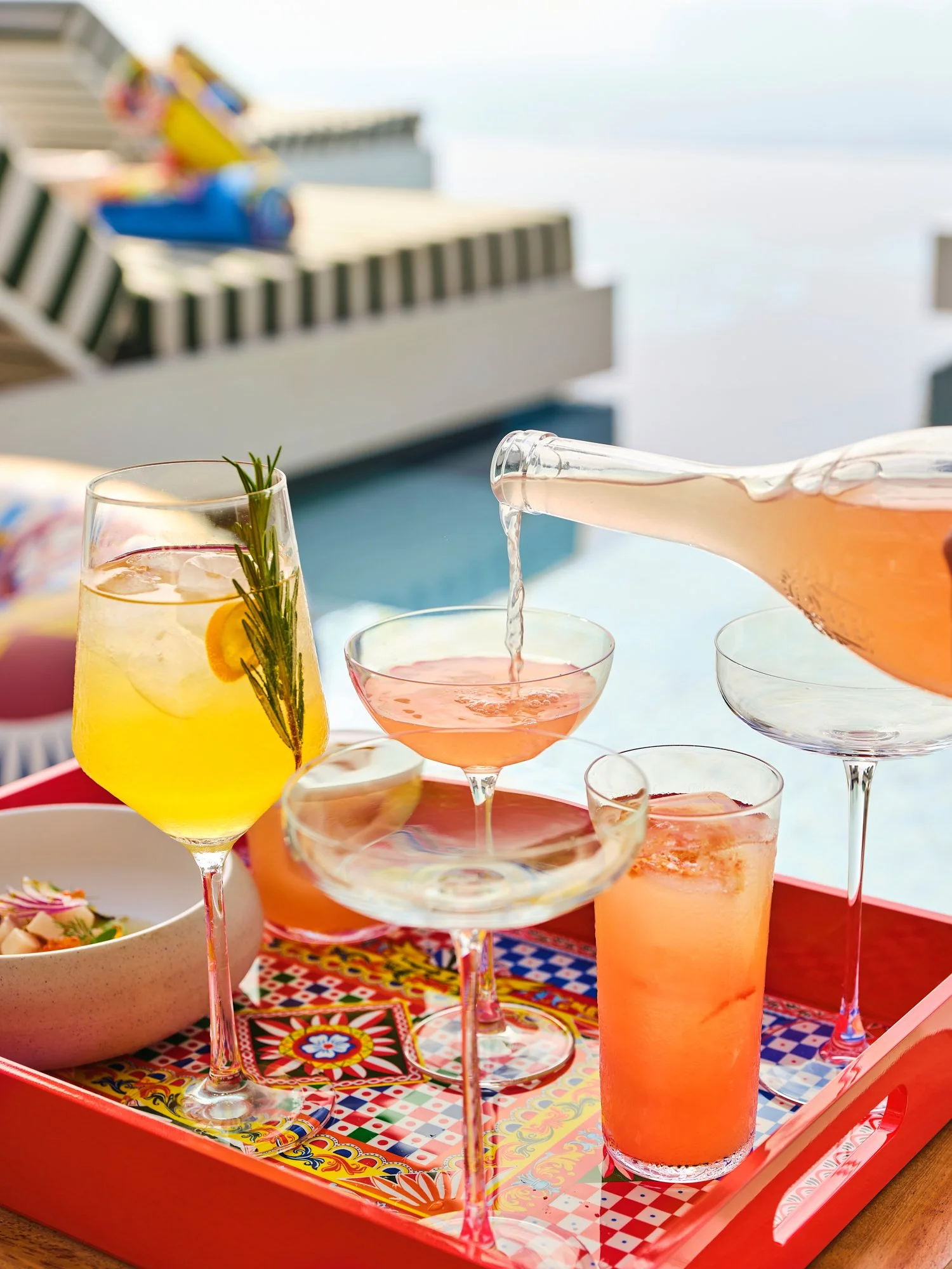 Colorful cocktails and drinks being served on a red tray by a poolside with a blurred pool background.
