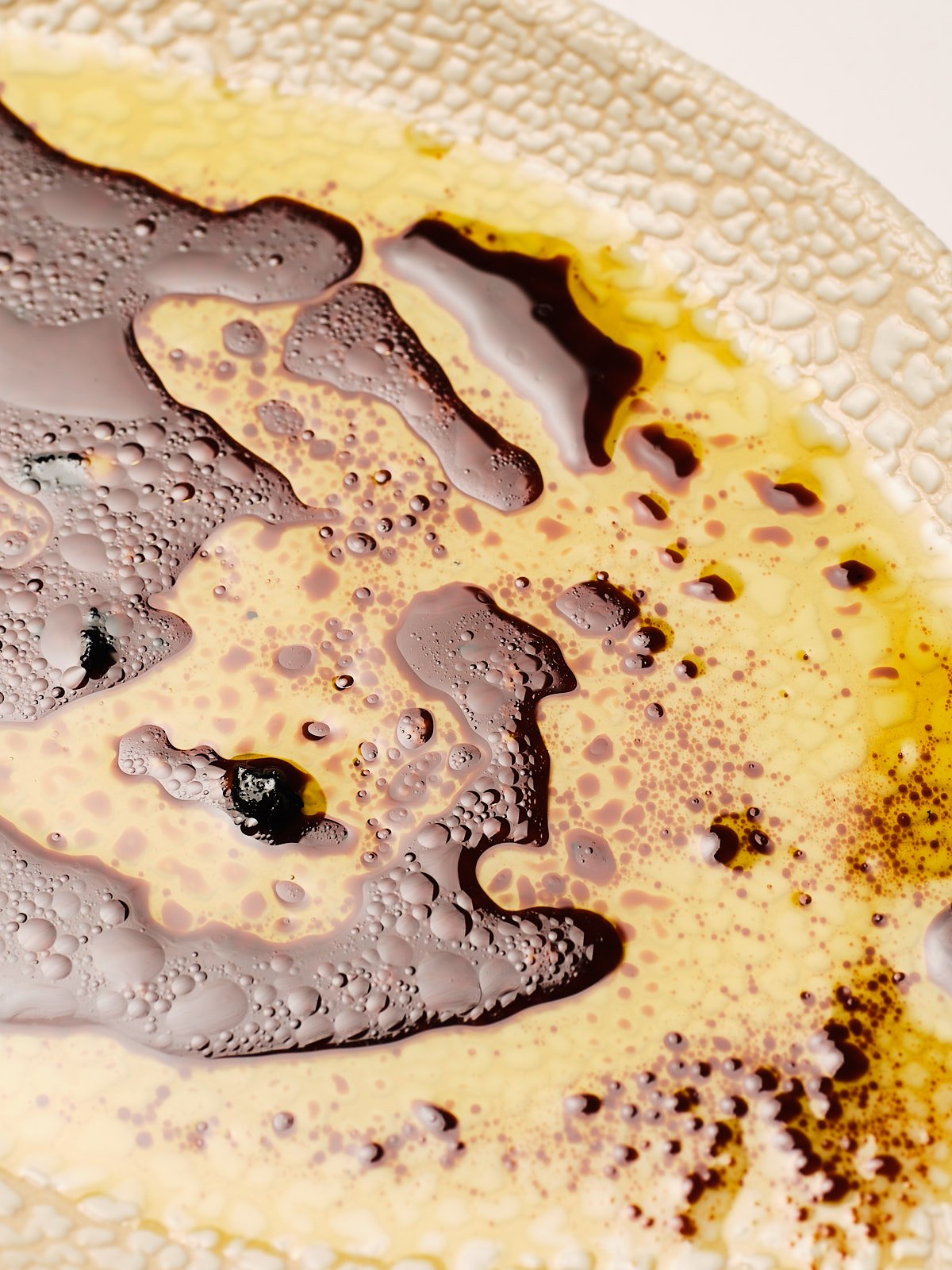Close-up of a textured surface with dark liquid and yellowish foam, possibly a close-up of a beverage like coffee or soda with bubbles.