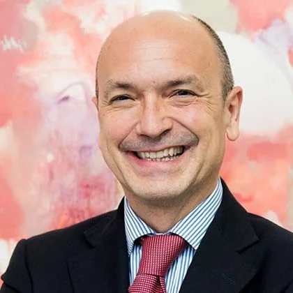 Portrait of a smiling man in a suit and tie standing in front of a colorful abstract background.