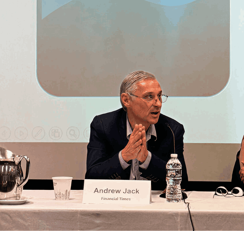 A man named Andrew Jack speaking at a conference table with a nameplate that reads 'Andrew Jack, Financial Times.' Behind him, a large screen displays a logo with the words 'Ma Ki' and a stylized blue and gray background, with the text 'MaKi Media Confer...' at the top.