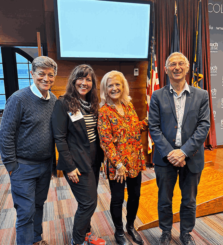 Four people standing together at a conference, with a screen behind them that reads "MaKi Media Conference NYC December 2024" and displays logos for MaKi and Baruch College Zicklin School of Business. The group includes two men and two women, all smiling, with flags in the background.