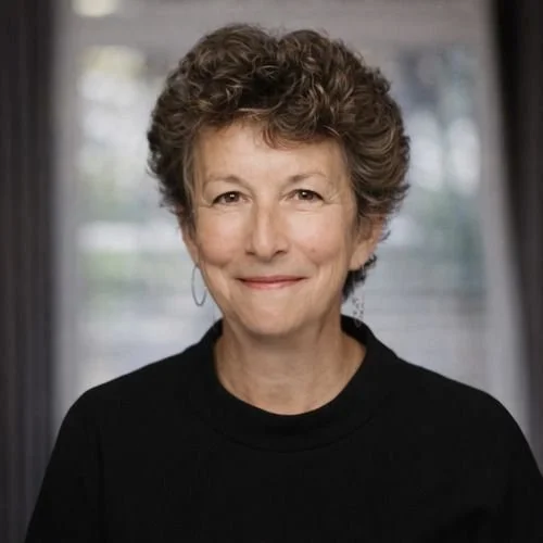 A woman with short, curly gray hair smiling in front of a window.