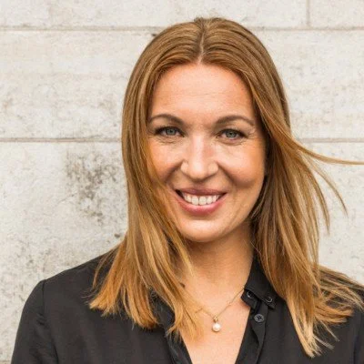 Close-up of smiling woman with long red hair wearing a black top and pearl necklace.