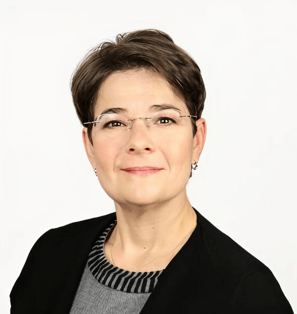A woman with short brown hair wearing glasses, a black blazer, and a striped shirt smiling against a white background.