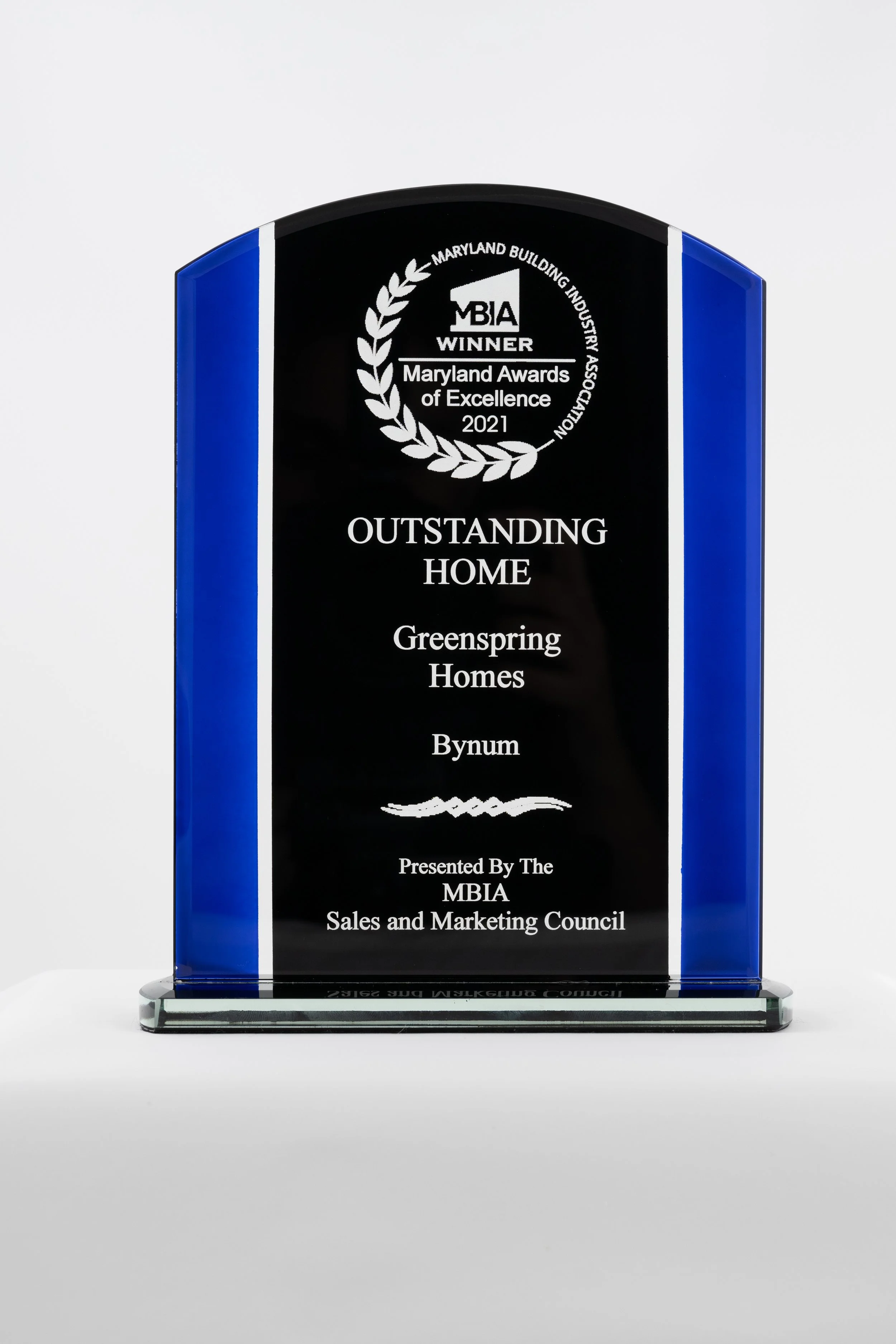 A glass award plaque with blue sides, recognizing Gre Spring Homes in Bynum as Outstanding Home of the Year, presented by the Maryland Building Industry Association Sales and Marketing Council in 2021.