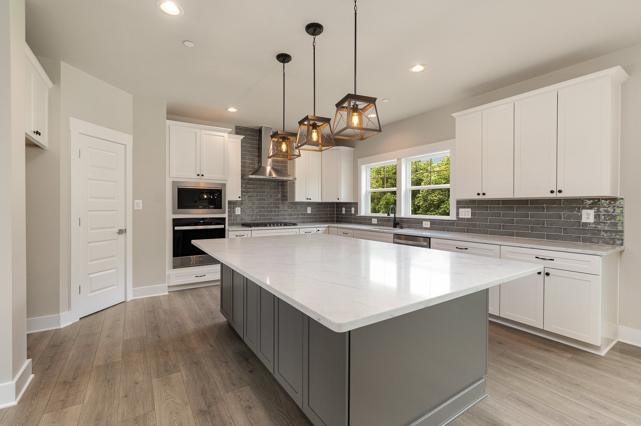 Modern kitchen with white cabinets, gray island, gray subway tile backsplash, stainless steel appliances, and pendant lights.