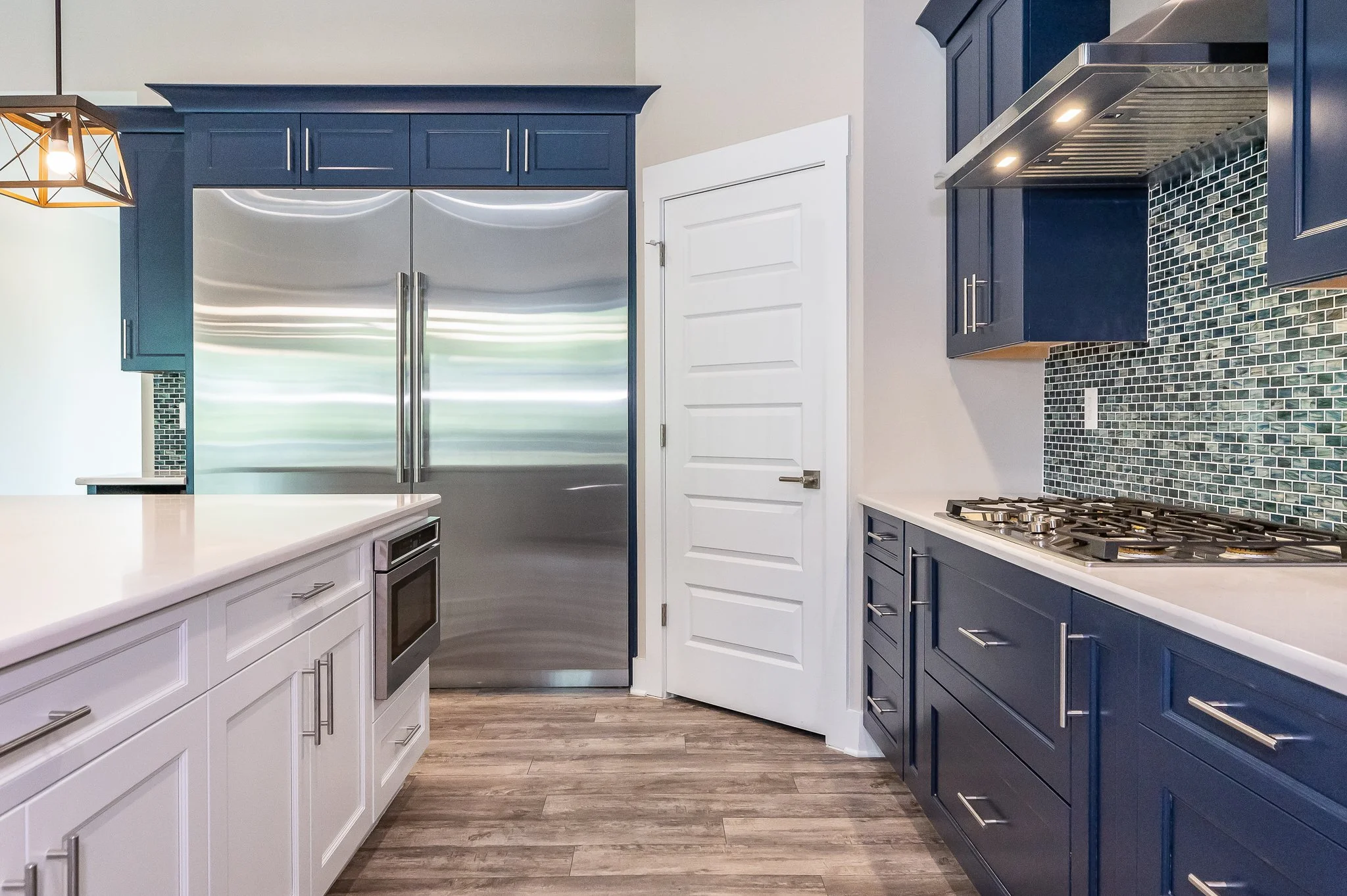 Modern kitchen with white and navy blue cabinetry, stainless steel refrigerator, gas stove, and mosaic tile backsplash.