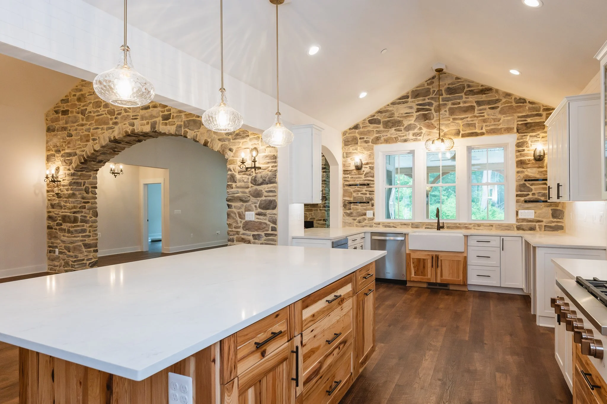 Modern kitchen with stone accent walls, white cabinets, a large island with a white countertop, and multiple pendant lights.
