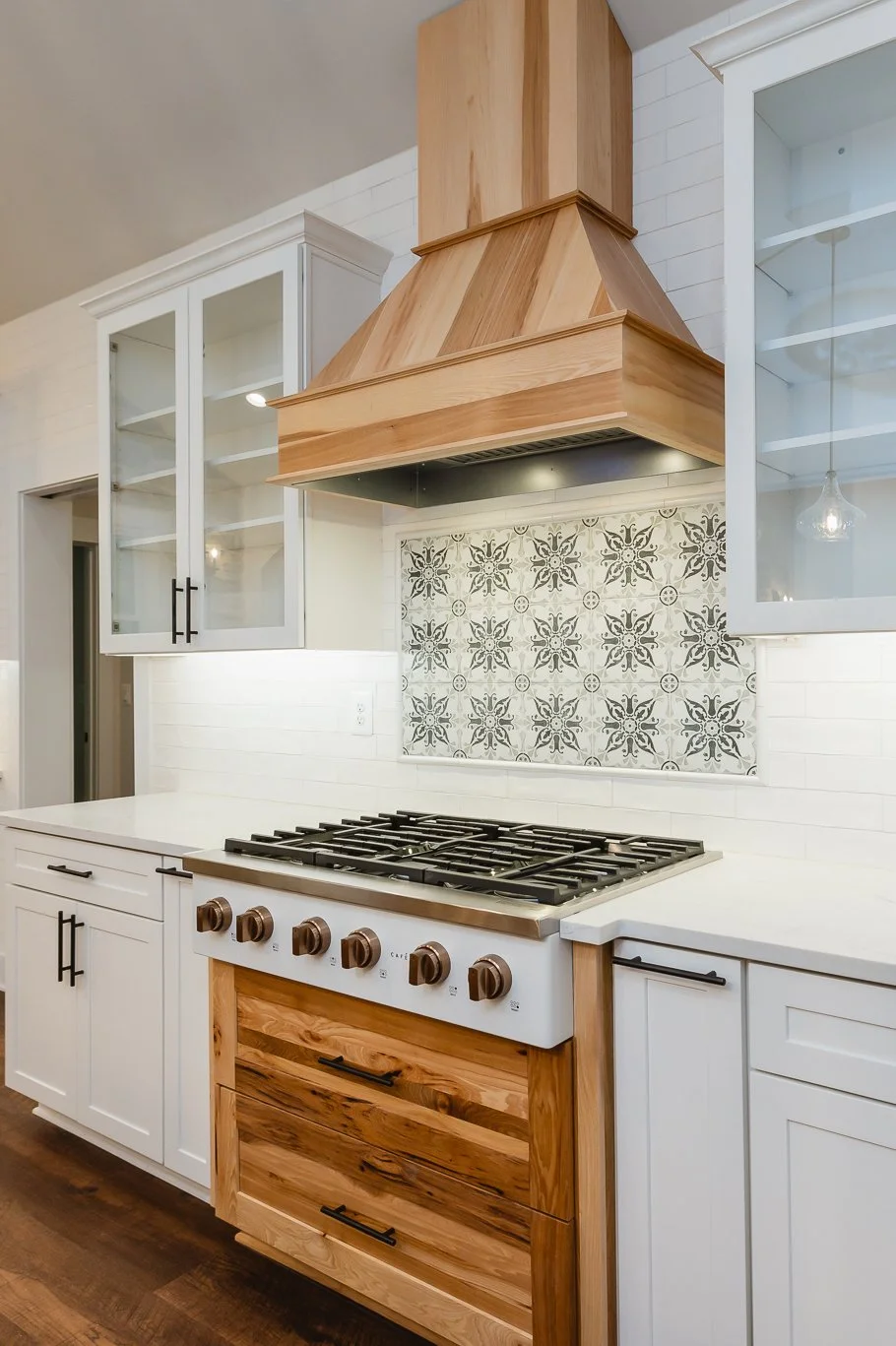 Kitchen with white cabinets, a wooden range hood, a patterned tile backsplash, and a gas stove.