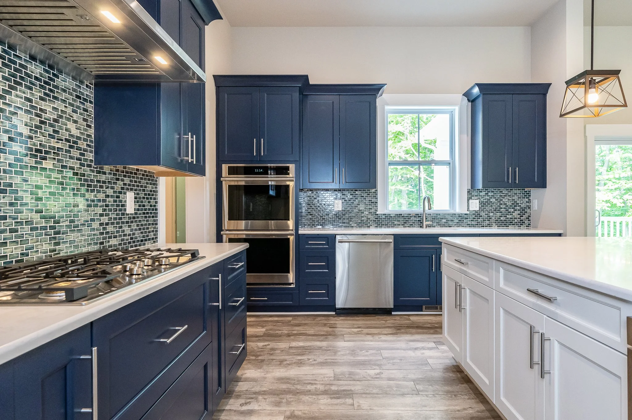 Modern kitchen with blue and white cabinets, mosaic tile backsplash, stainless steel appliances, and a window over the sink.