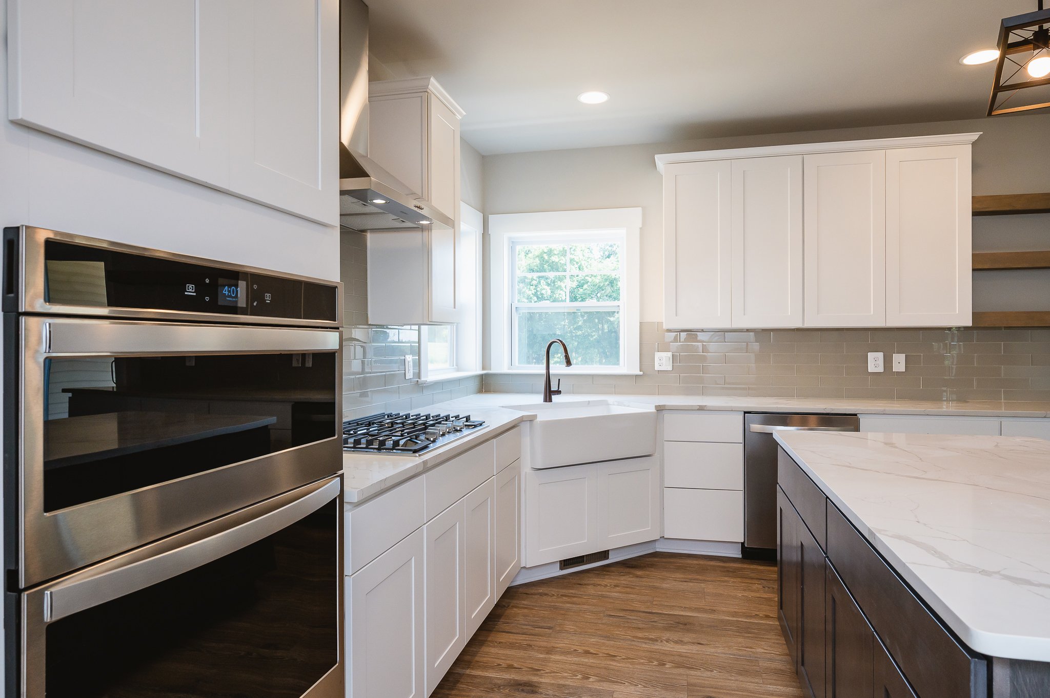 Modern kitchen with white cabinets, a window above the sink, a stainless steel oven, and a kitchen island with a marble countertop.