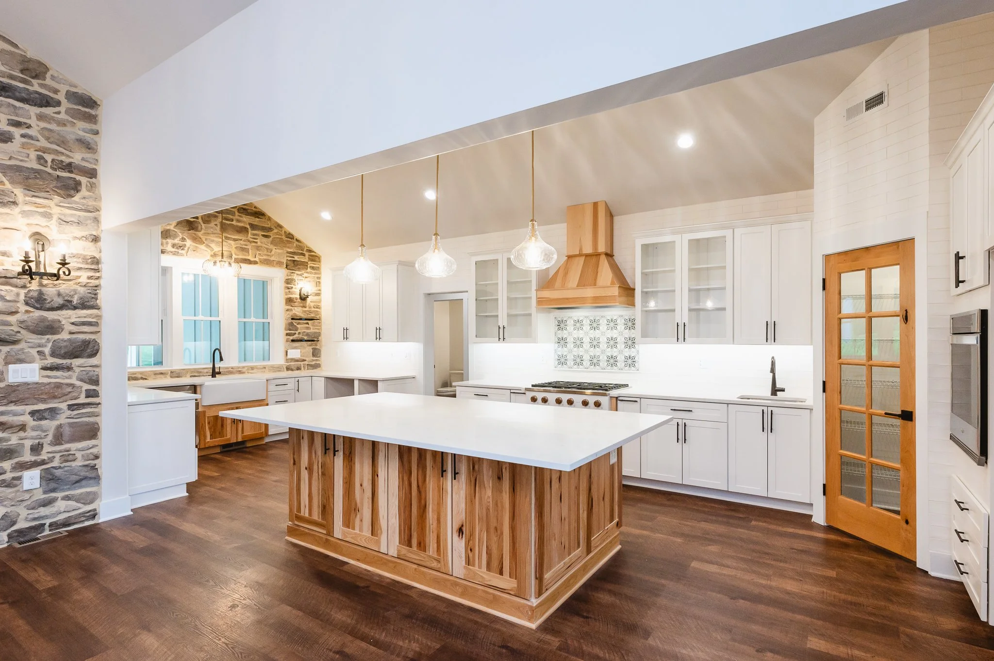 Modern kitchen with white cabinets, a wooden island, stone accent wall, and wooden accents around doors and appliances.