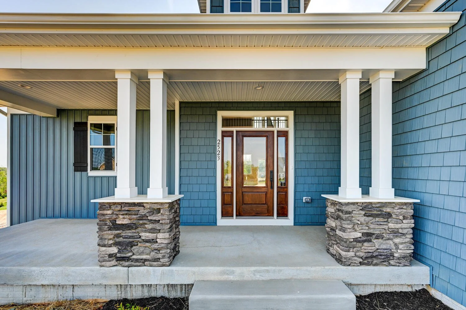 Front view of a blue house with stone pillars, a wooden front door, and a covered porch.