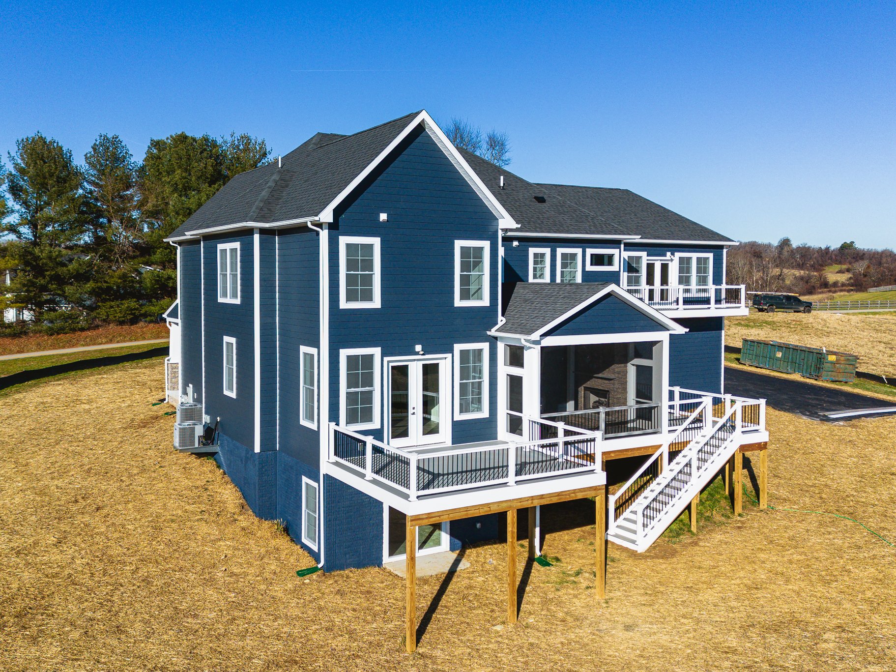 A large blue multi-story house with white trim, multiple windows, and a screened-in porch with stairs on a grassy yard under a clear blue sky.