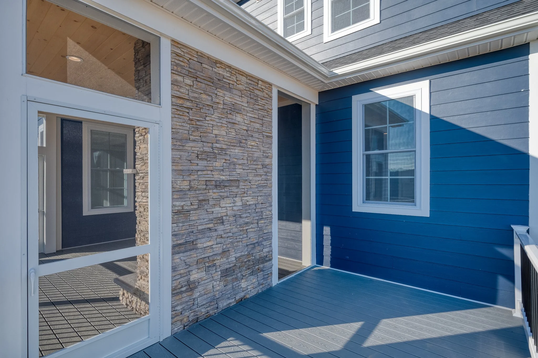 Exterior view of a house with blue siding, white-framed windows, a stone accent wall, and a glass door leading to a deck.