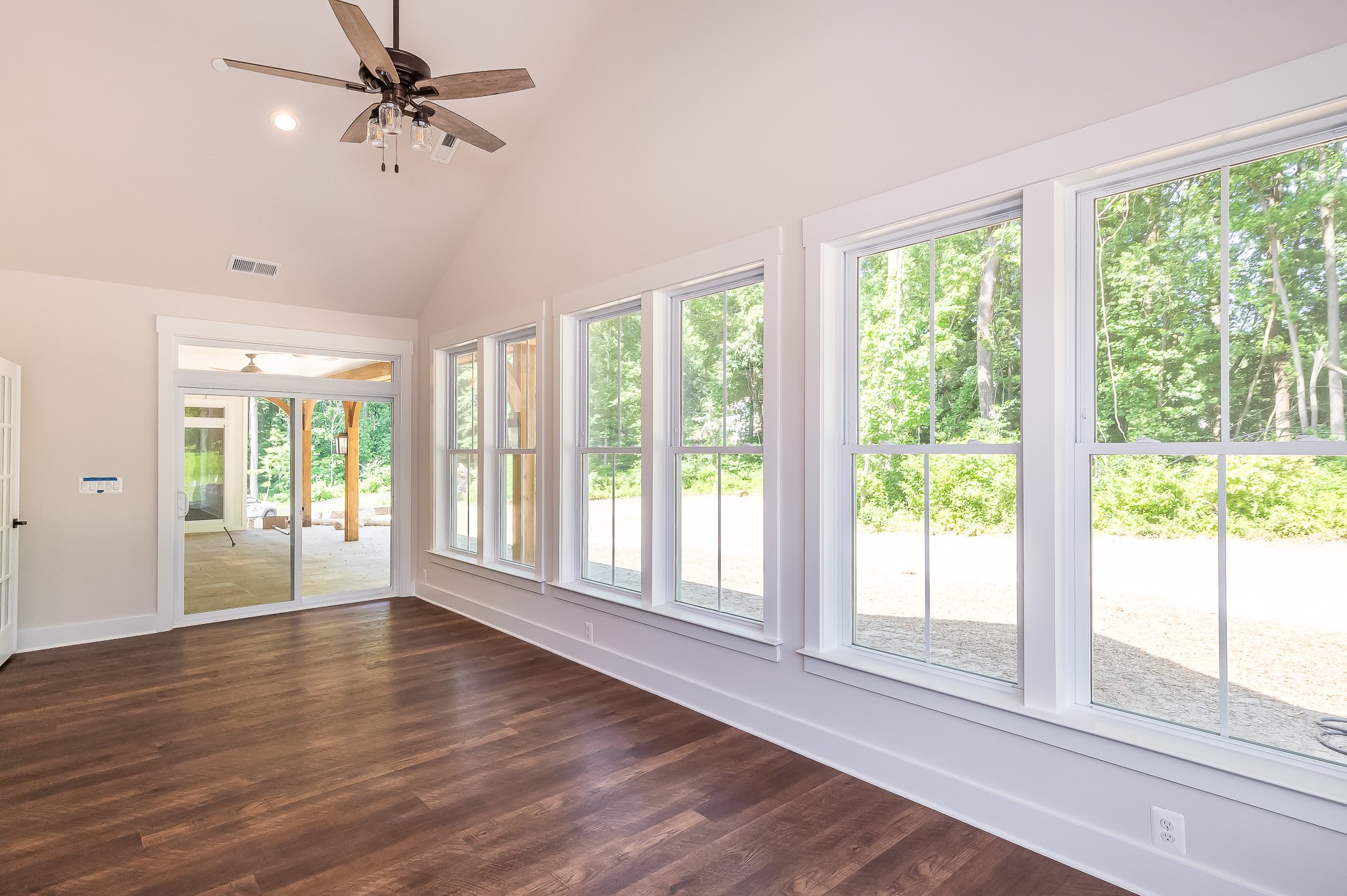 Empty room with wood flooring, large windows, a ceiling fan, and a sliding glass door leading to an outdoor area.