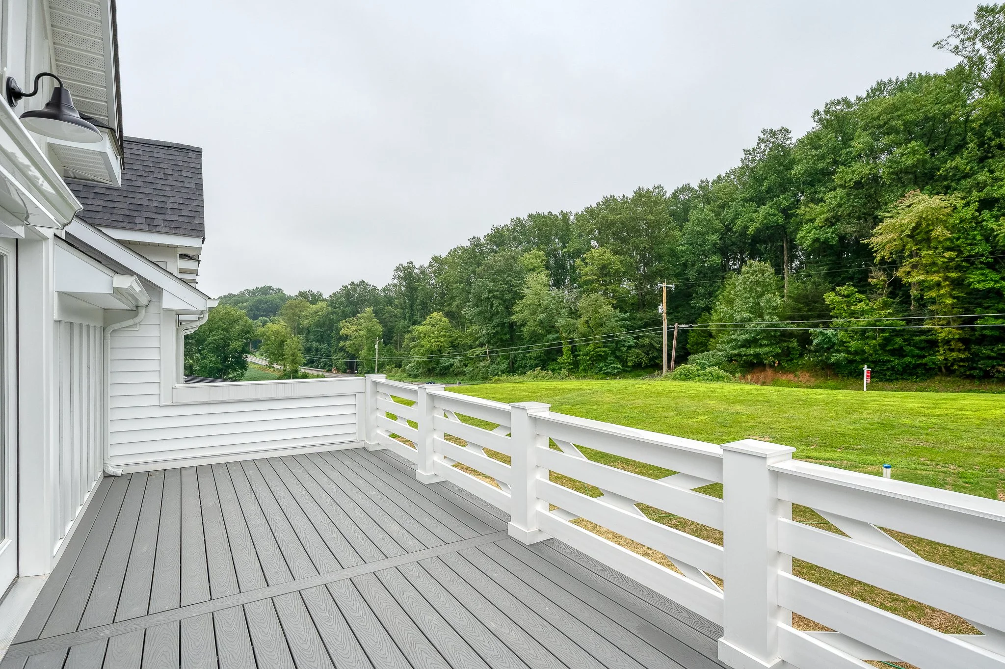 View from a gray wooden deck with white railing overlooking a grassy yard and trees beyond.