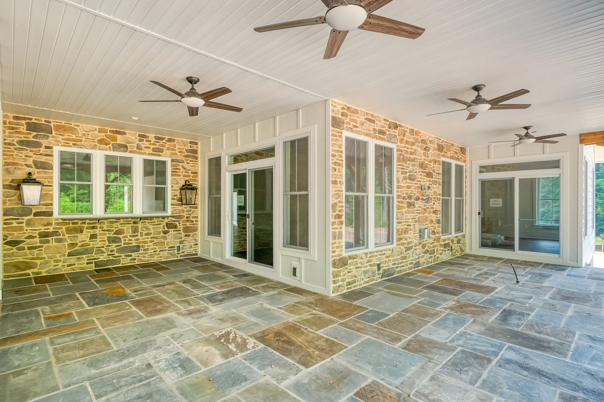 Spacious screened porch with stone flooring, brick walls, white trim, ceiling fans, and large windows with screens.
