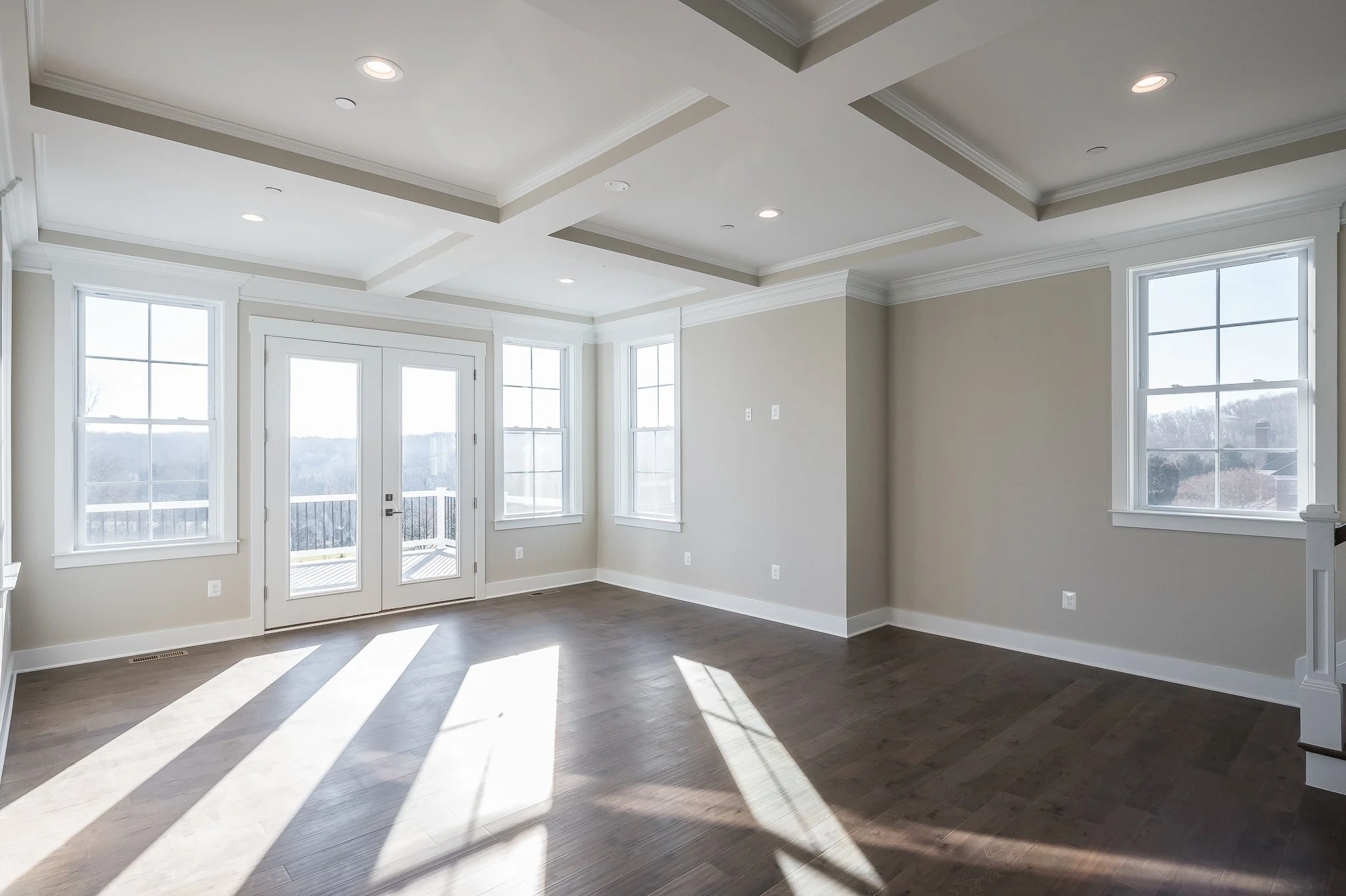 Empty living room with large windows and door leading outside, hardwood flooring, and ceiling with recessed lighting.
