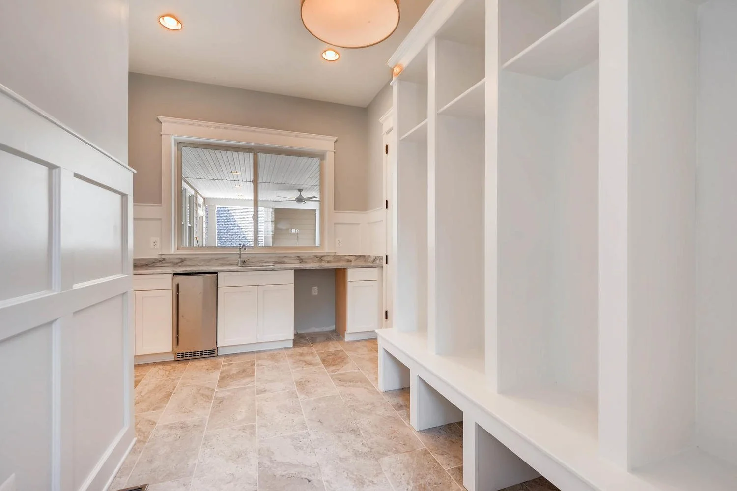 Empty laundry room with white cabinets, marble countertop, window, and tiled floor.
