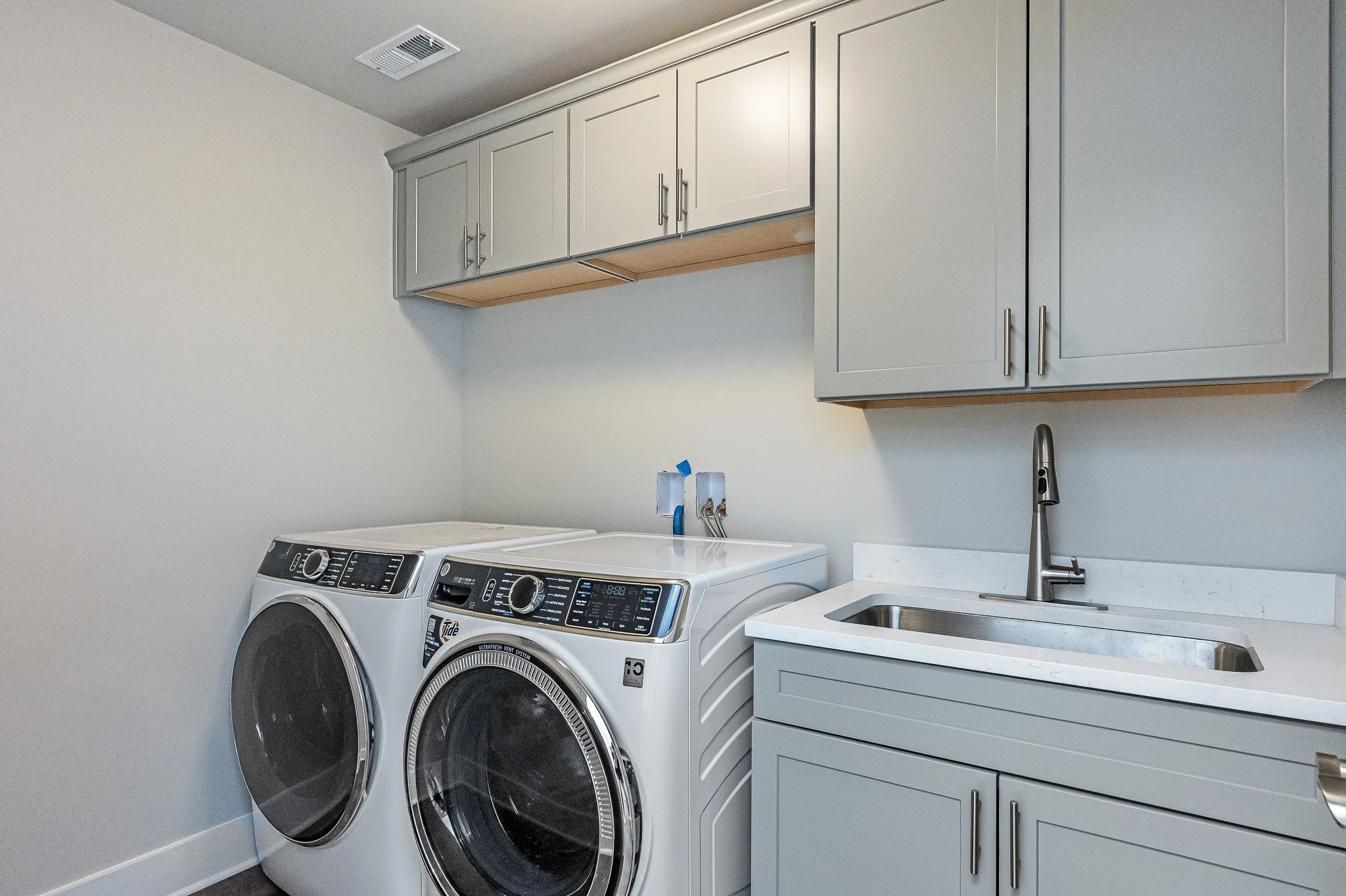 Laundry room with a washing machine, a dryer, a sink, and overhead cabinets.