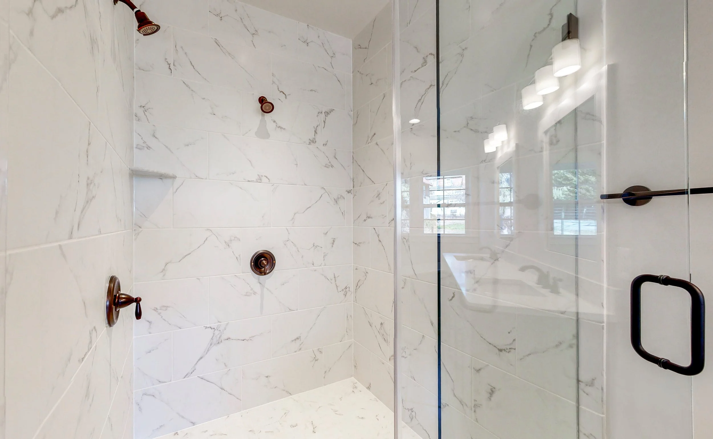 Modern shower with white marble tiles, bronze fixtures, and a glass door.