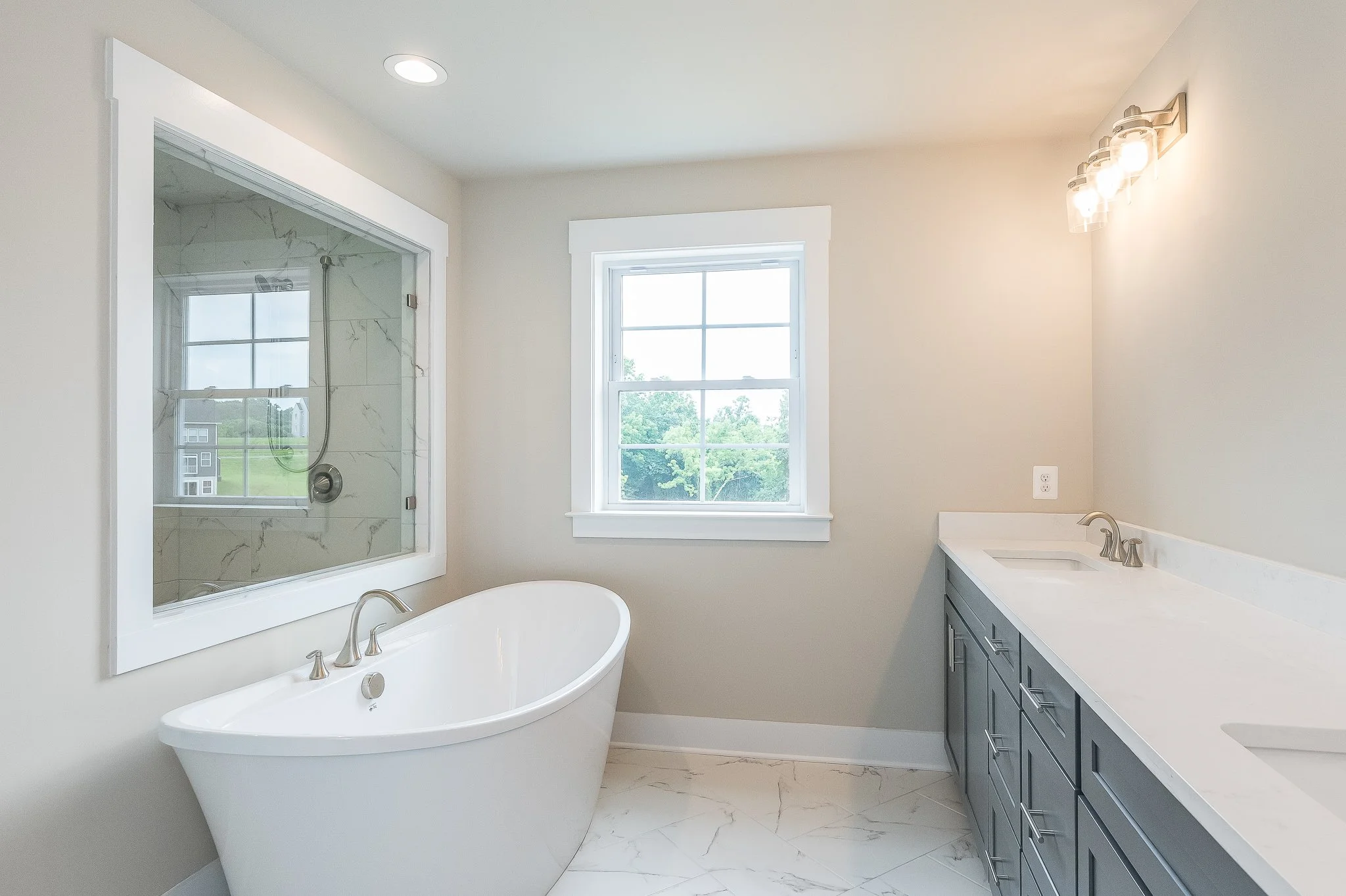 Bathroom with a standalone bathtub, large window, and a double vanity with gray cabinets and white countertops.