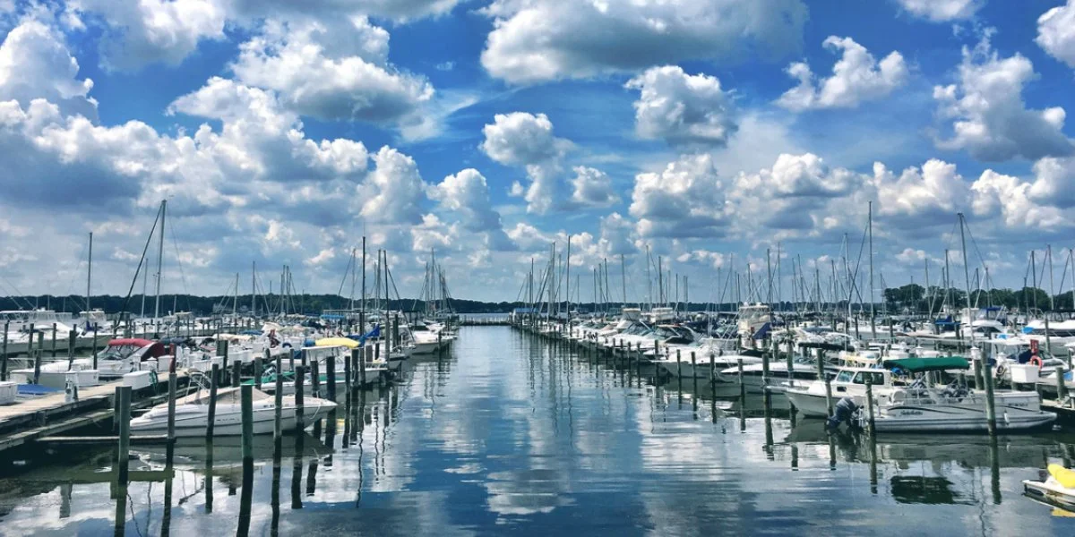 A marina filled with boats docked along the piers under a partly cloudy sky reflected in the calm water.