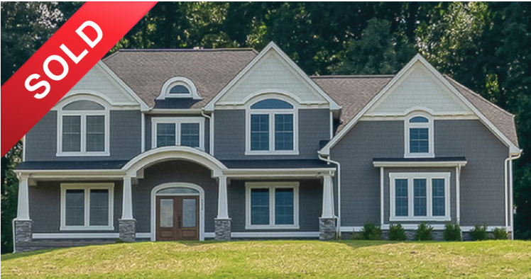 Front view of a two-story house with blue siding, multiple gables, and a large front porch, marked sold with a red banner.