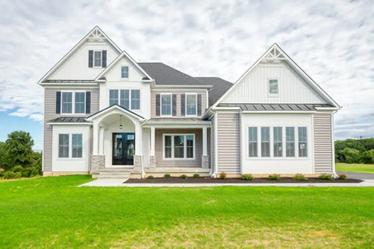 A large, modern two-story house with a front porch, surrounded by a well-maintained lawn and partly cloudy sky.