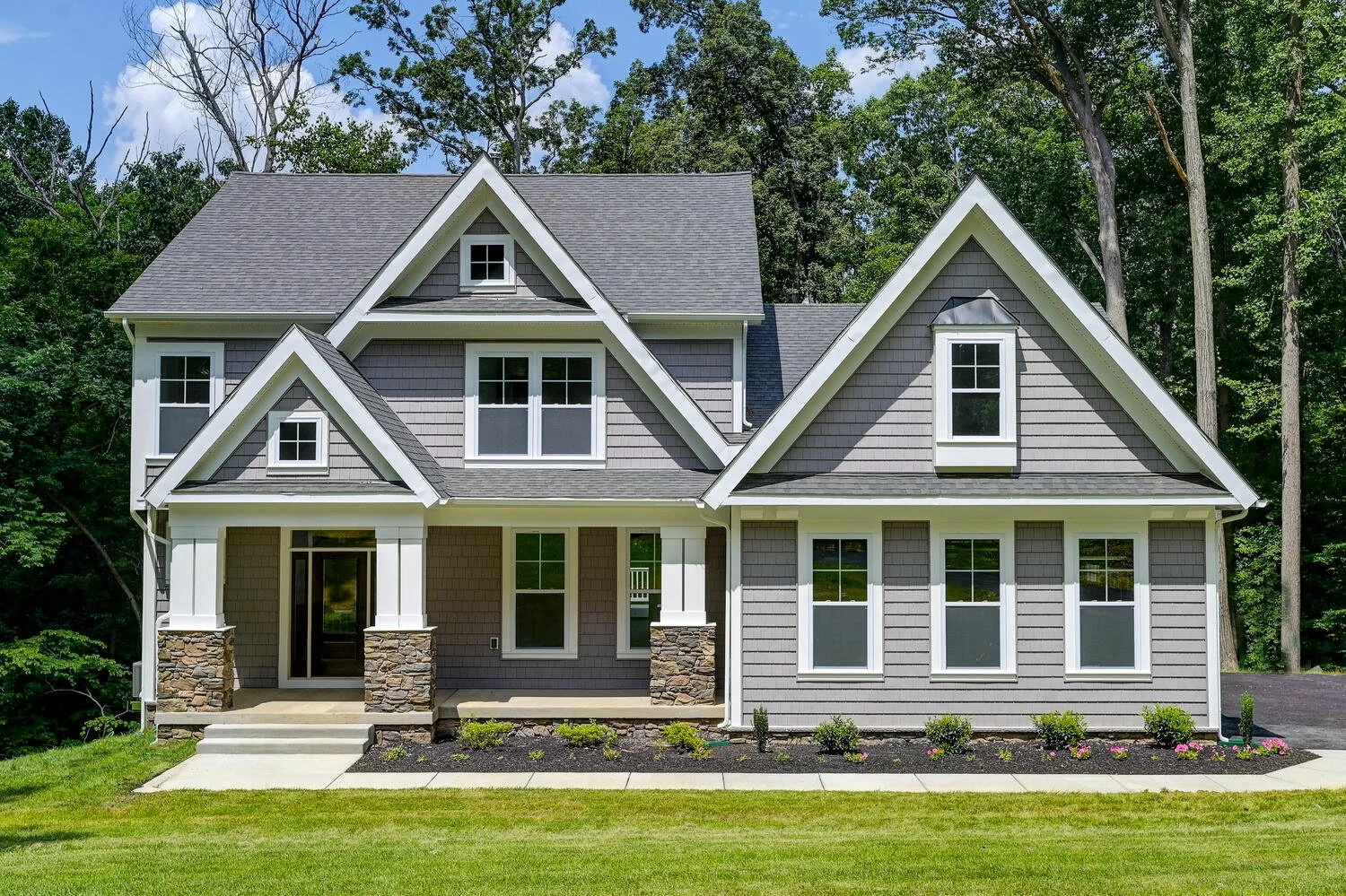 A modern two-story house with gray siding and white trim, surrounded by a well-maintained lawn and trees in the background.
