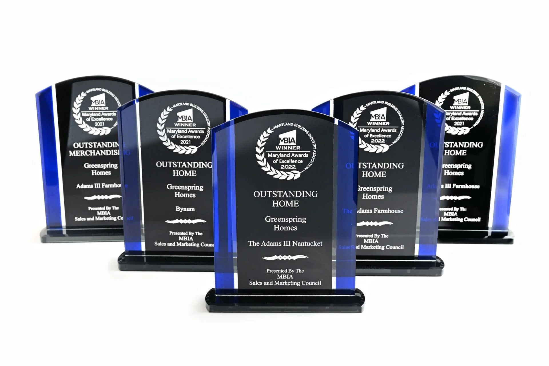 Five glass awards with black background and blue accents, inscribed with recognition for Greenspring Homes and The Adams III Nantucket, presented by the MBIA Sales and Marketing Council.