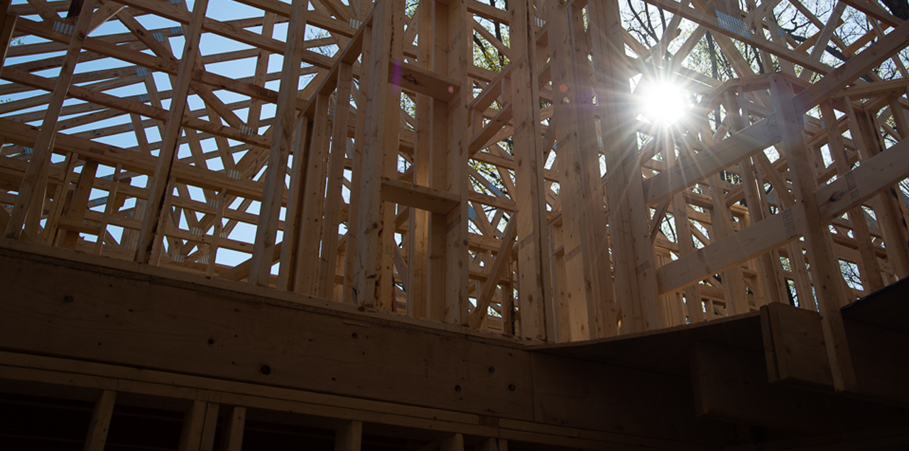 Wooden framing of a building under construction with sunlight shining through the structure.