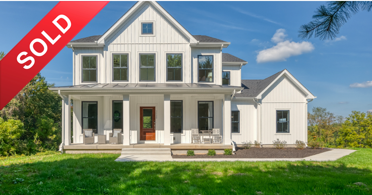 A newly sold two-story white house with front porch and multiple windows, set on a green lawn with trees in the background and a partly cloudy sky.