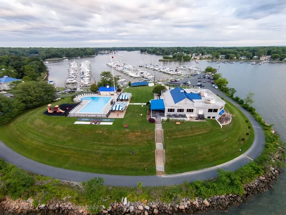 Aerial view of a lakeside property with a house, swimming pool, poolside umbrellas, and a boat marina in the background.