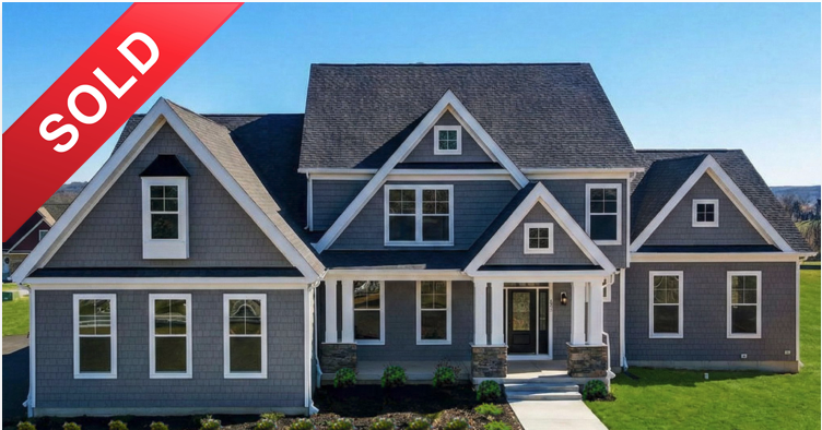 Newly built gray house with multiple gables, white trim, and front porch, marked sold, on a sunny day