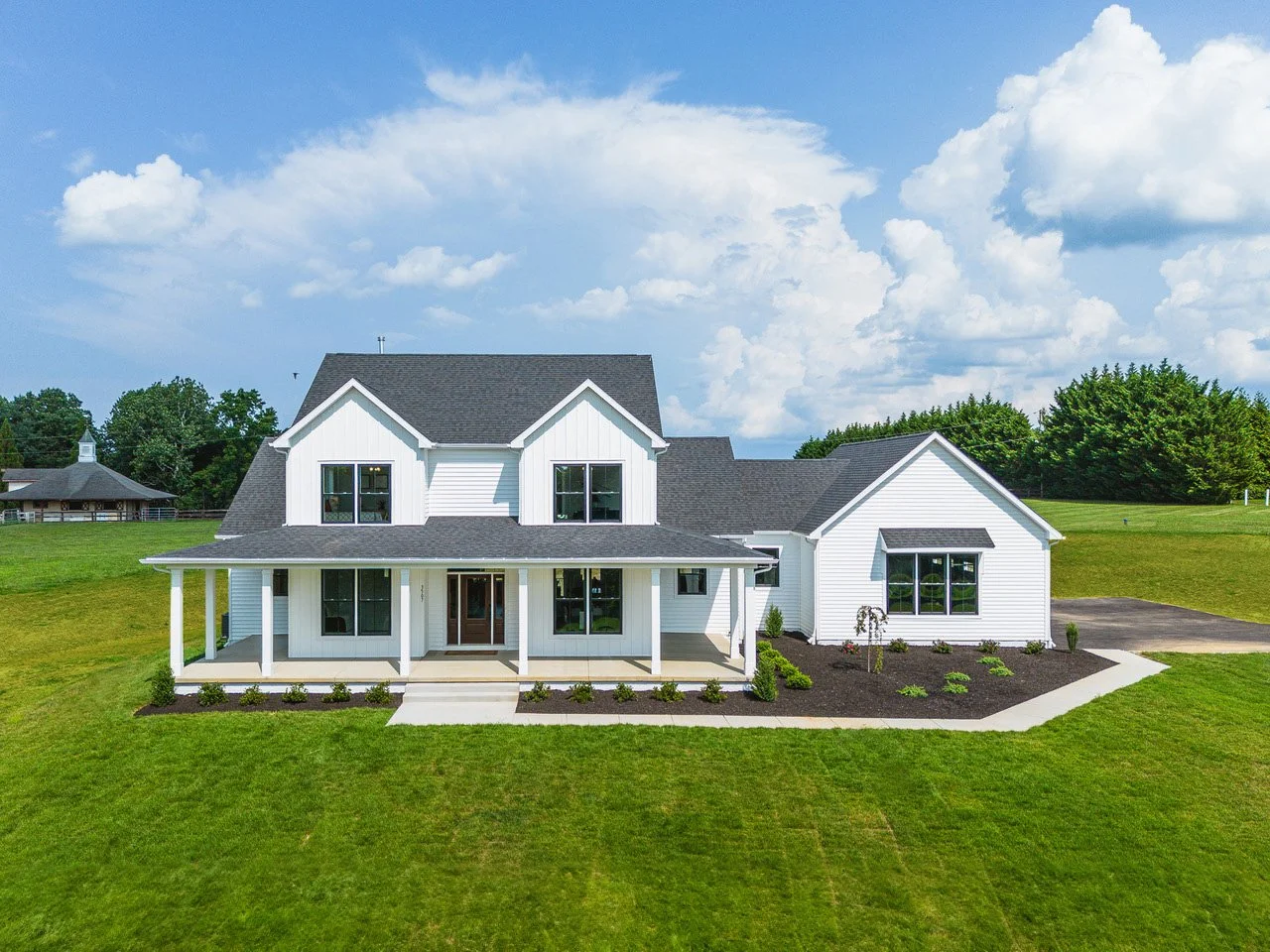 Front view of a modern white two-story house with a porch, black windows, and a landscaped front yard with green grass and small plants, under a partly cloudy sky.