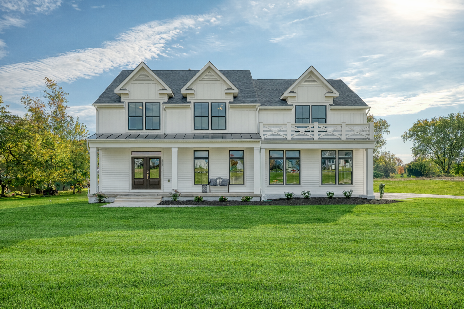 A large white two-story house with black doors and many windows, set on a well-maintained lawn with trees in the background.
