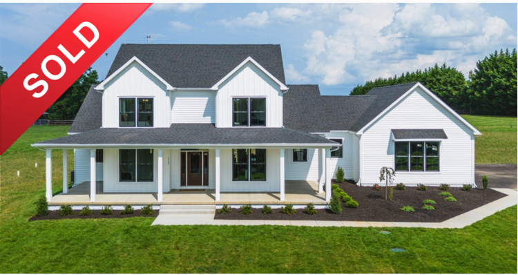 New white two-story house with dark roof and front porch, sold sign in the top left corner.