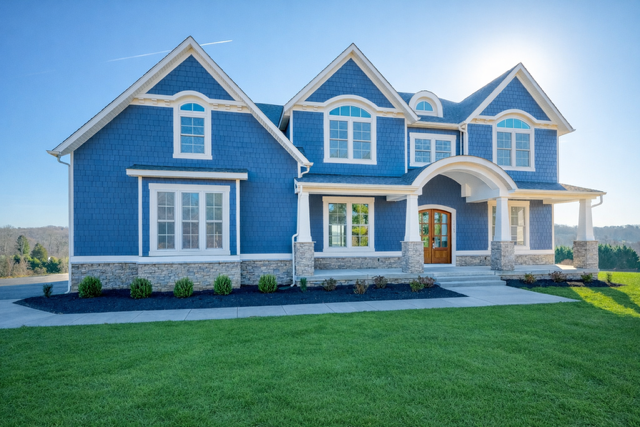 A large blue two-story house with white trim, stone accents, a front porch with columns, and a well-maintained green lawn.