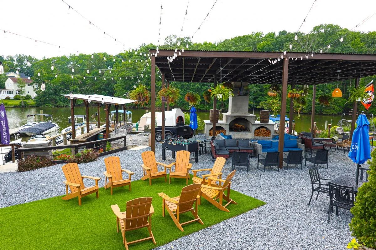 Outdoor lakeside patio with seating, string lights, a fireplace, and boat docks in the background.